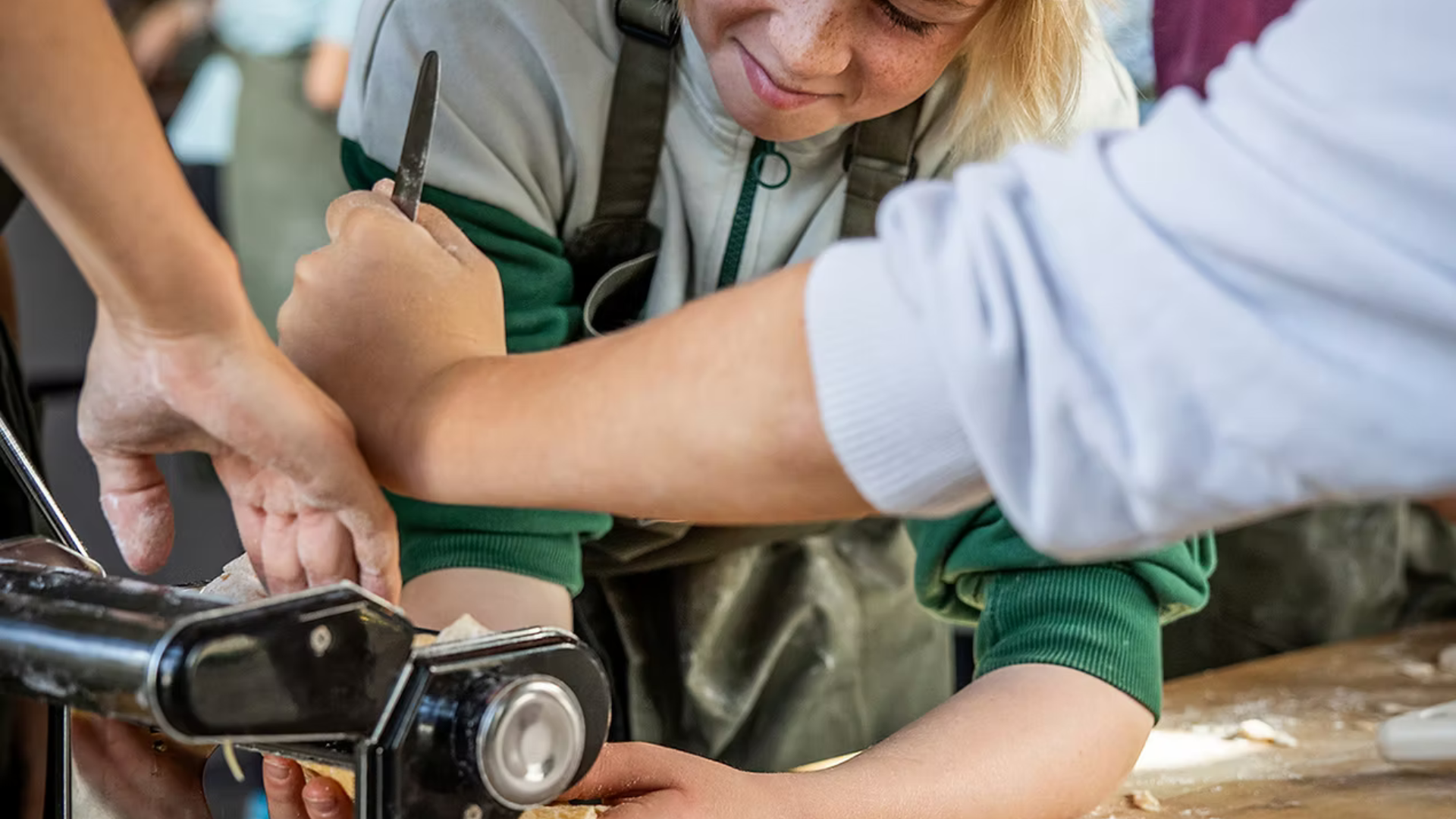 Ein Mädchen macht Nudeln und dreht den Teig gerade durch eine Nudelmaschine