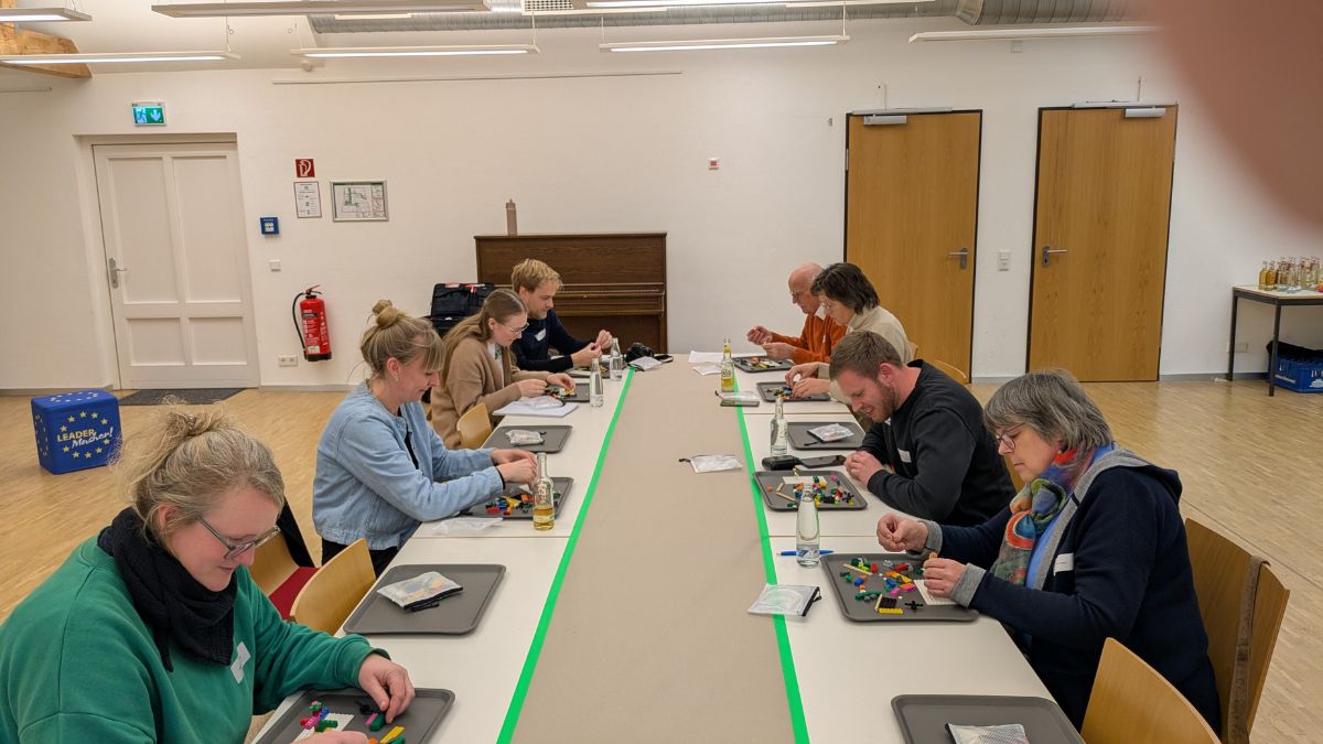 8 Personen sitzen vor Lego-Steinen und bauen etwas